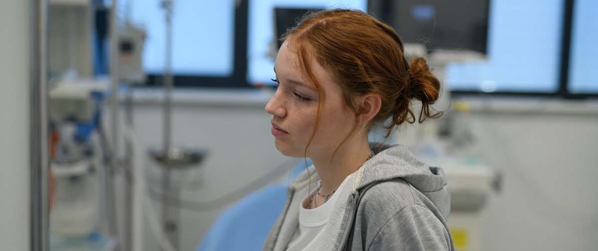 Eine junge Frau mit nachdenklichem Gesichtsausdruck in einer Notaufnahme.